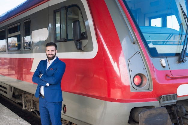 Portrait of professional train driver standing by high speed train vehicle at station