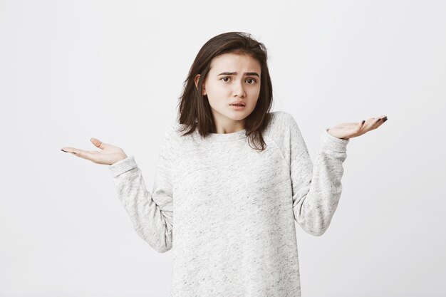 portrait of puzzled and clueless young adult shrugging her shoulders and raising hands showing perplexed gesture