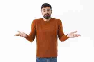 Free photo portrait of puzzled and unaware attractive bearded man shrugging with hands spread sideways dont know what do standing indecisive need help with decision cant understand white background