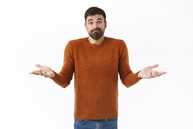 Portrait of puzzled and unaware attractive bearded man shrugging with hands spread sideways dont know what do standing indecisive need help with decision cant understand white background