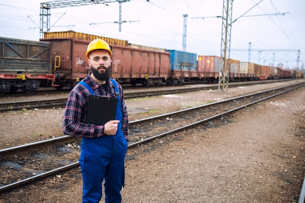 Портрет рабочего-железнодорожника с буфером обмена, стоящего у железнодорожных путей и грузового поезда на заднем плане