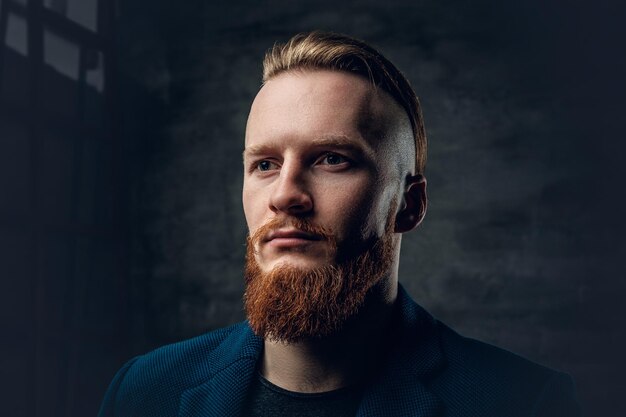 Portrait of redhead bearded hipster male dressed in a blue jacket over grey background.