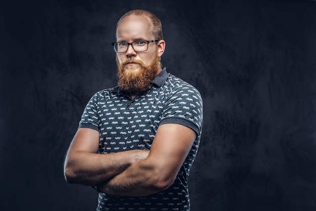 Portrait of a redhead bearded male dressed in a t-shirt posing with crossed arms. Isolated on a dark textured background.