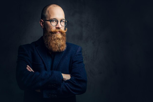 Portrait of redhead bearded male in eyeglasses dressed in an elegant wool suit over grey background.