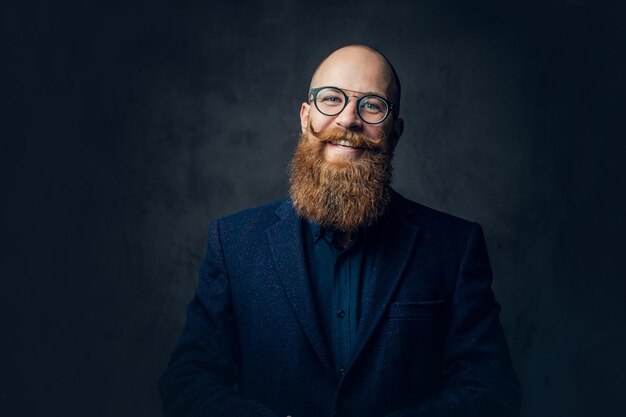 Portrait of redhead bearded male in eyeglasses dressed in an elegant wool suit over grey background.