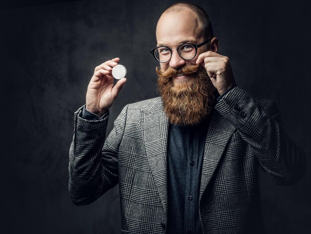 Portrait of redhead bearded male in eyeglasses dressed in an elegant wool suit over grey background.