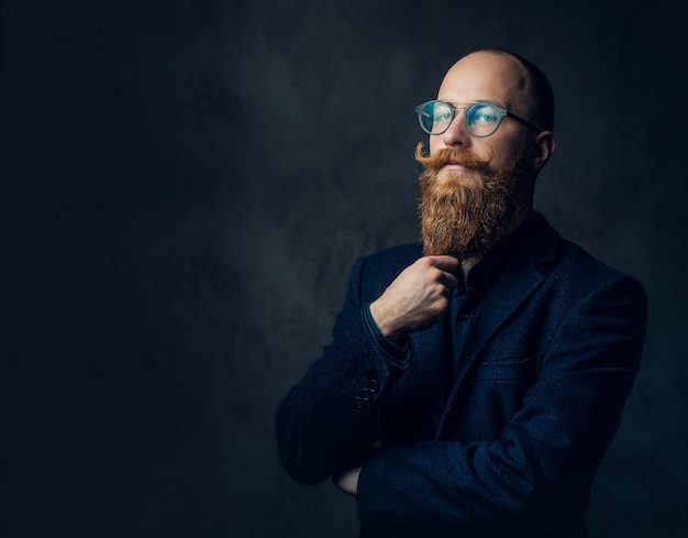 Portrait of redhead bearded male in eyeglasses dressed in an elegant wool suit over grey background.