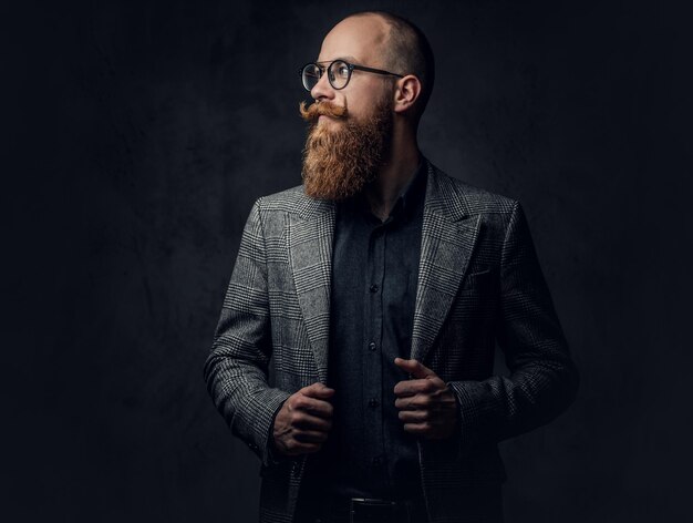 灰色の背景の上にエレガントなウールのスーツを着た眼鏡の赤毛のひげを生やした男性の肖像画。