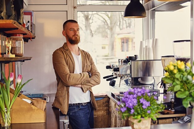 花とコーヒーマシンがたくさんある小さなカフェで赤毛のひげを生やした男性の肖像画。