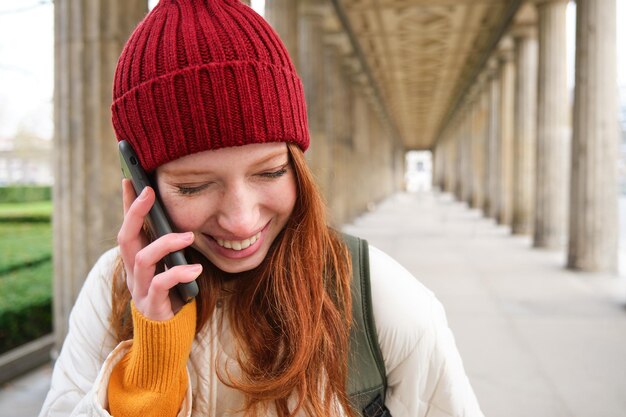 빨간 모자를 쓴 빨간 머리 유럽 소녀의 초상화는 도시에서 전화를 걸고 친구와 이야기합니다.