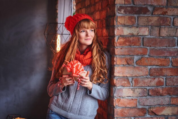 Portrait of redhead female in a warm clothes holds Christmas gift.