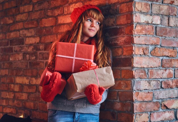 따뜻한 옷을 입은 빨간 머리 여성의 초상화가 크리스마스 선물을 들고 있습니다.