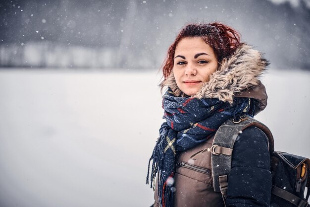 Portrait of a redhead girl with a backpack walking through winter forest