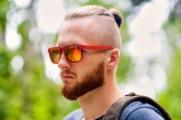 Портрет рыжеволосого мужчины в солнечных очках над диким городским парком.