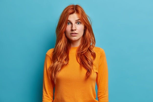 Портрет рыжеволосой молодой женщины смотрит с удивлением, а в повседневном оранжевом джемпере удивляет лицо.