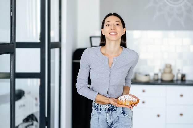 喜んでいる女性の肖像画は、家でおいしいクロワッサンを食べます。不健康な食品の概念。