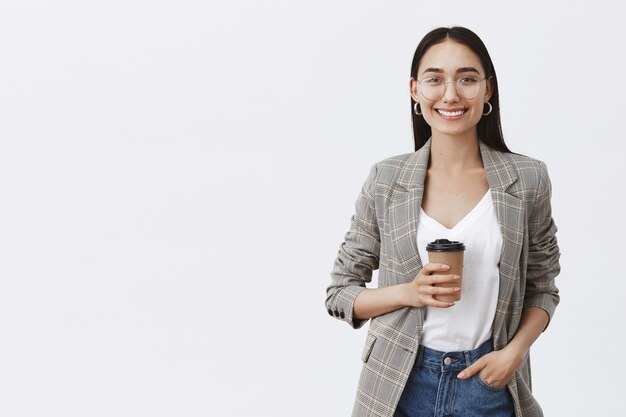 Portrait of relaxed and confident european woman with dark hair and glasses, holding hand in pocket and drinking tea