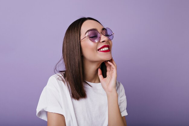 Portrait of relaxed european woman with bright makeup laughing with eyes closed.  Indoor photo of pleasant white woman in sunglasses isolated.