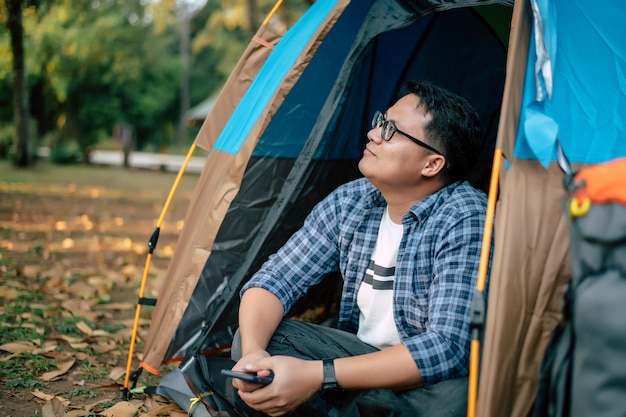 Портрет расслабляющего азиатского путешественника в очках, смотрящего на вид, сидя в палаточном кемпинге Открытый кемпинг и концепция образа жизни