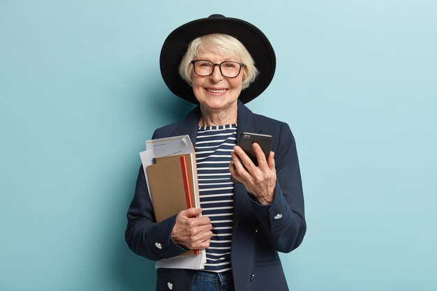 Portrait of retired teacher with grey hair, wrinkled skin, carries papers and notebook