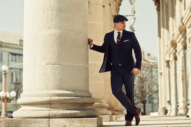 Portrait of retro 1920s english arabian business man wearing dark suit tie and flat cap near old columns