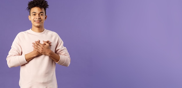 Foto gratuita il ritratto dell'uomo ispanico bello romantico con i dreadlocks tiene le mani premute al cuore e le suppliche sorridenti