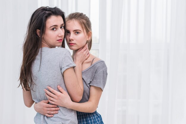 Portrait of a romantic young lesbian couple standing in front of white curtain