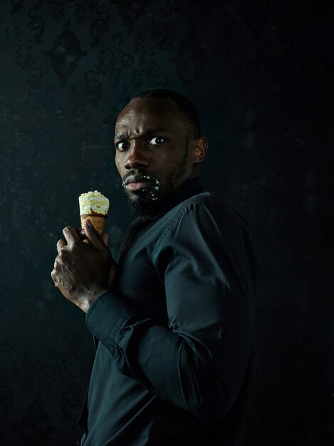 Portrait of sad afro american man holding ice cream over black studio background