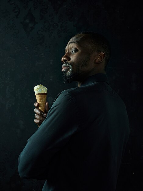 검은 스튜디오 배경 위에 아이스크림을 들고 슬픈 아프리카 미국 남자의 초상화