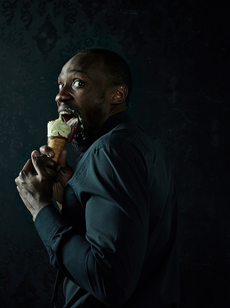 Ritratto di uomo afroamericano triste che tiene il gelato sopra il fondo nero dello studio