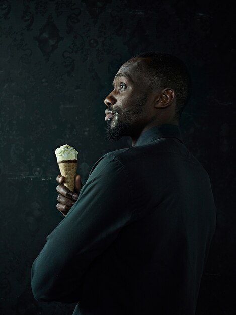 Portrait of sad afro american man holding ice cream over black studio background