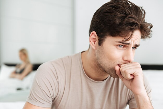 Portrait of sad brunette man sitting in bed at home