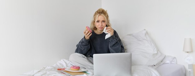 Portrait of sad and depressed woman feeling heartbroken lying in bed with comfort food eating