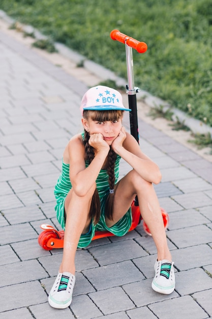 Portrait of a sad girl wearing cap sitting on red push scooter