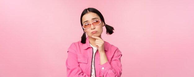 Portrait of sad and gloomy asian girl sulking from disappointment standing upset against pink studio background Copy space