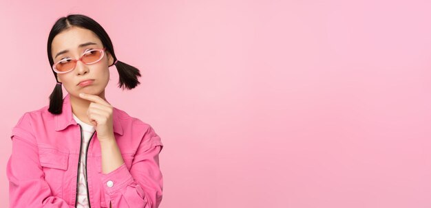 Portrait of sad and gloomy asian girl sulking from disappointment standing upset against pink studio background