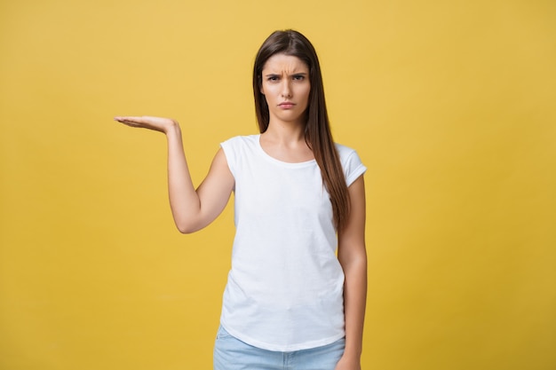 Portrait of sad and serious girl holding holding a hand aside. isolated on yellow background.