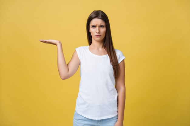 Portrait of sad and serious girl holding holding a hand aside. Isolated on yellow background.