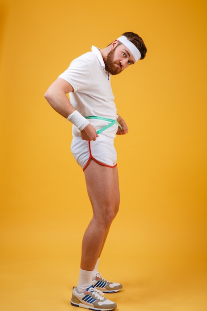 Портрет грустного неудовлетворенного человека фитнеса измеряя его тело