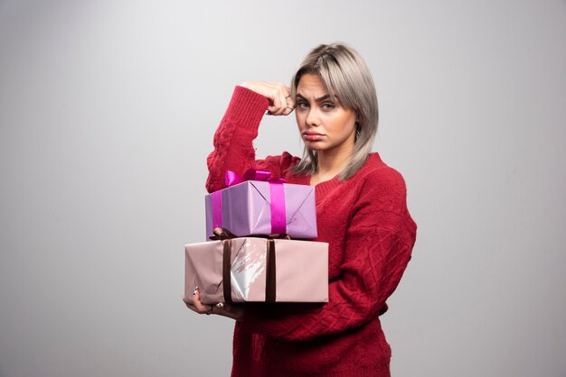 Portrait of sad woman holding gift boxes on gray background.