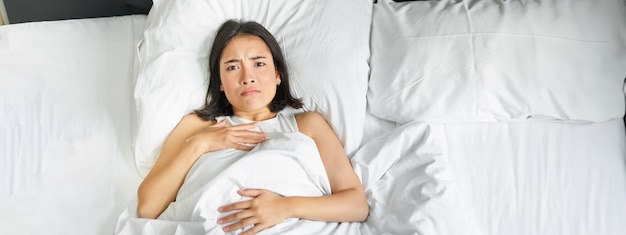 Free photo portrait of sad young asian woman lying in bed overthinking before going to sleep stay late because