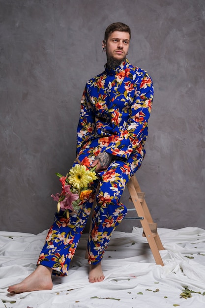 Портрет грустный молодой человек, сидя на стуле с букетом цветов в руке