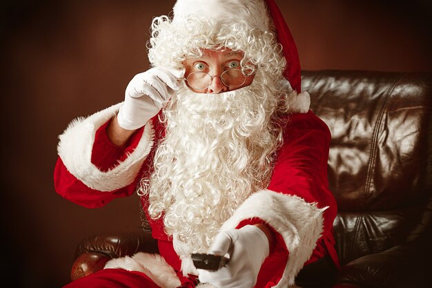 Portrait of Santa Claus in red costume with TV remote control