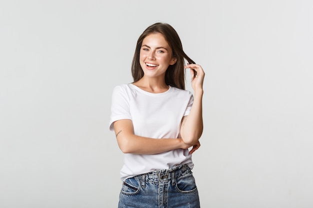 Portrait of sassy attractive young woman, playing with hair strand and smiling satisfied.