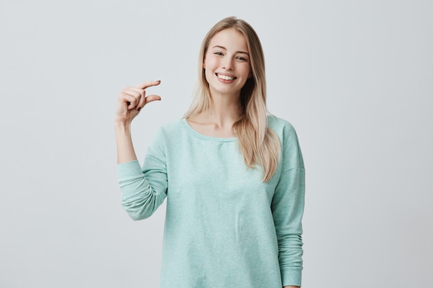 portrait of satisfied happy caucasian female model with blonde smiling broadly demonstrating size of something