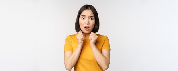 Portrait of scared asian woman shaking from fear looking terrified and concerned standing anxious against white background