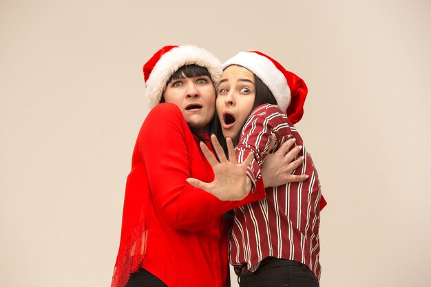 A portrait of a scared mother and daughter in Santa hat on gray