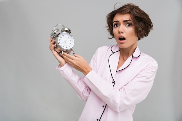 Free photo portrait of a scared woman in pajamas holding alarm clock