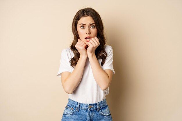 Portrait of scared woman trembling watching smth scary and looking insecure timid posing against bei...