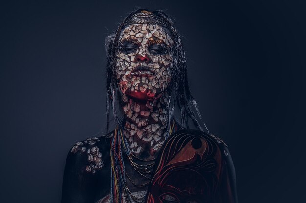 어두운 배경에 석화 금이 간 피부와 향취를 가진 무서운 아프리카 무당 여성의 초상화. 메이크업 개념입니다.